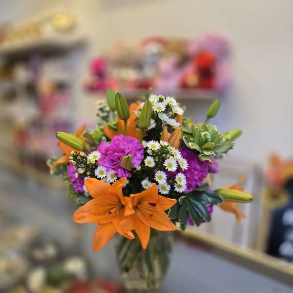 Bouquet of orange lilies, purple flowers, and white daisies in a glass vase