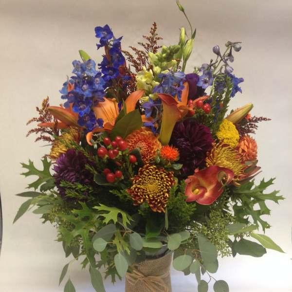 Colorful mixed bouquet with lilies, calla lilies, and chrysanthemums in a burlap-wrapped vase
