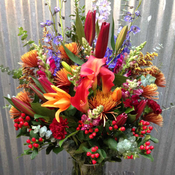 Tall mixed bouquet with lilies, calla lilies, and orange blooms in a glass vase