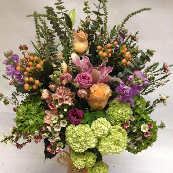 Mixed bouquet with roses, lilies, hydrangeas, and berries in a burlap-wrapped vase