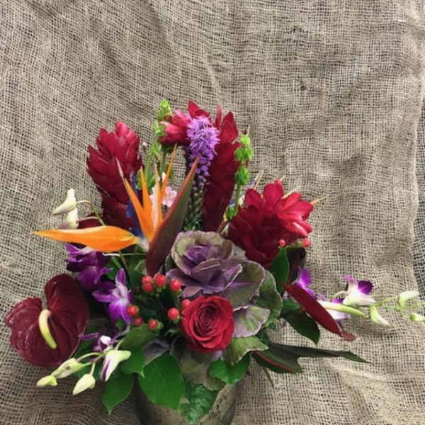 Mixed tropical bouquet in a low vase with red, purple, and orange blooms