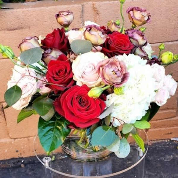 Low round arrangement of red and blush roses with white blooms in a clear glass vase