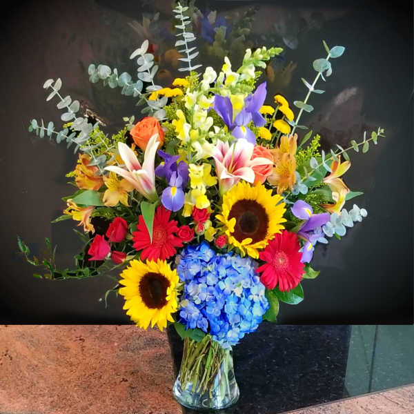 Colorful mixed bouquet with sunflowers, lilies, roses, and hydrangea in a glass vase