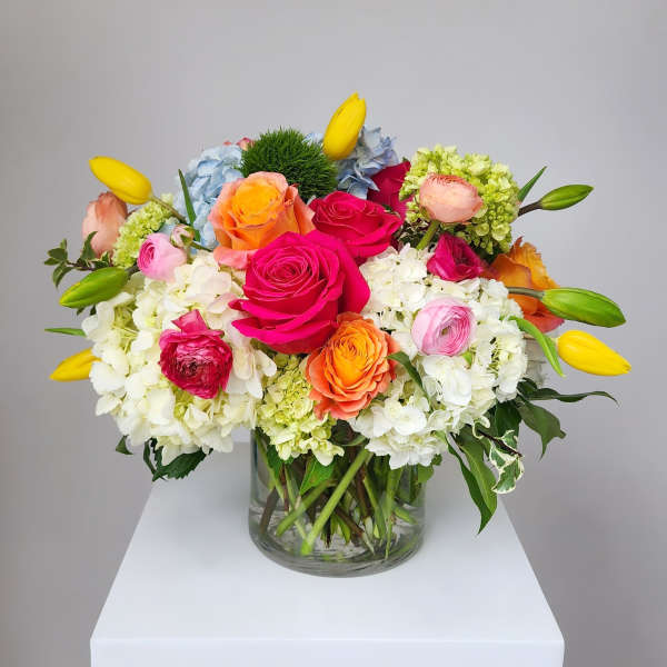 Colorful mixed bouquet in a clear glass vase with roses, hydrangeas, and tulips