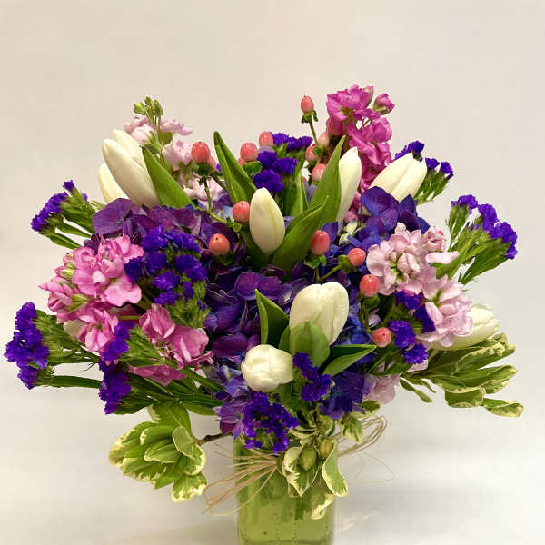 Colorful bouquet of tulips, purple blooms, and pink flowers in a green glass vase