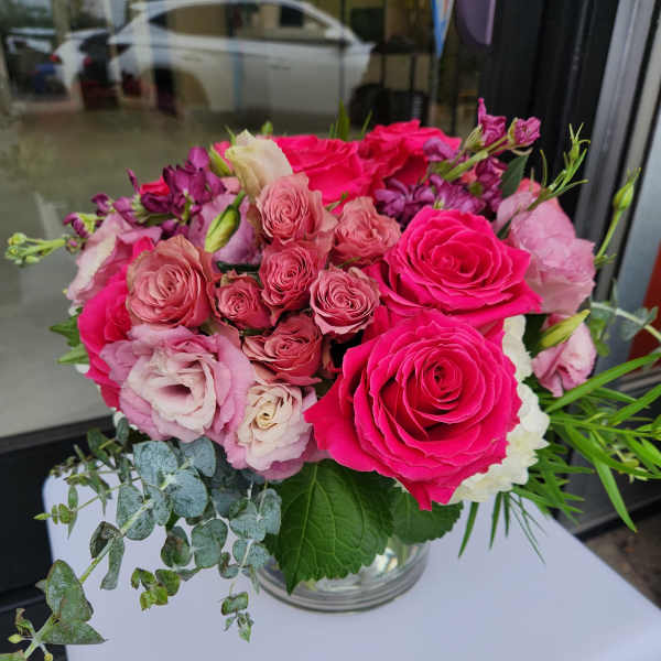 Low round arrangement of bright pink and blush flowers in a clear glass vase