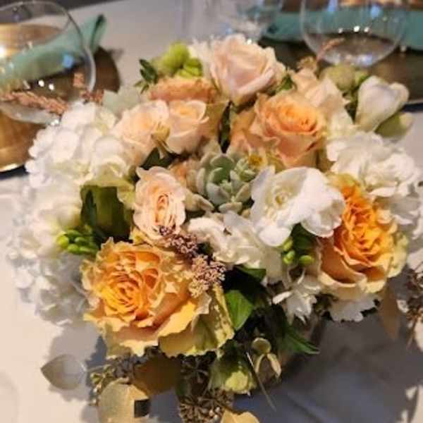 Low centerpiece of peach roses and white flowers in a clear glass vase