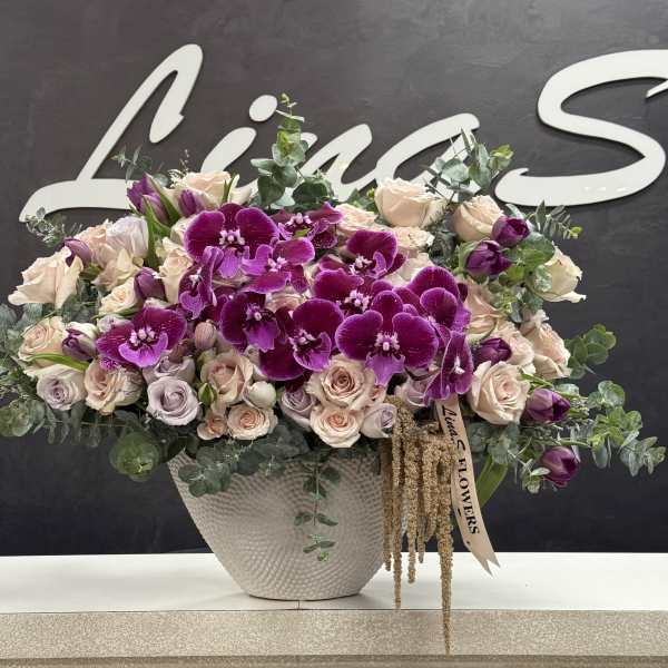 Large bouquet of purple orchids and pale roses in a textured white vase
