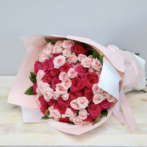 Large bouquet of light and hot pink roses wrapped in pale pink and white paper with ribbon
