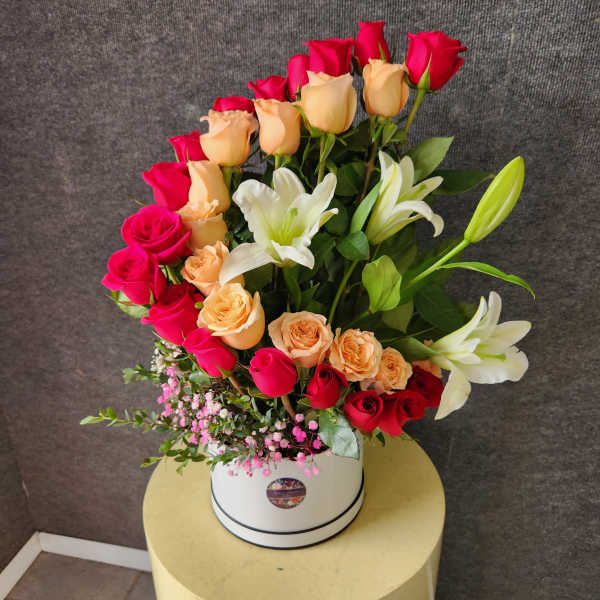 Bouquet of pink, peach, and white roses with white lilies in a white hat box