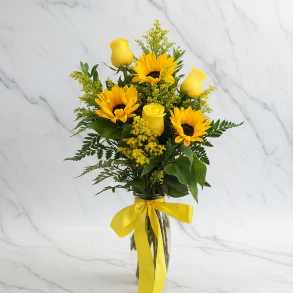 Tall arrangement of yellow sunflowers and roses in a clear vase with a yellow ribbon bow
