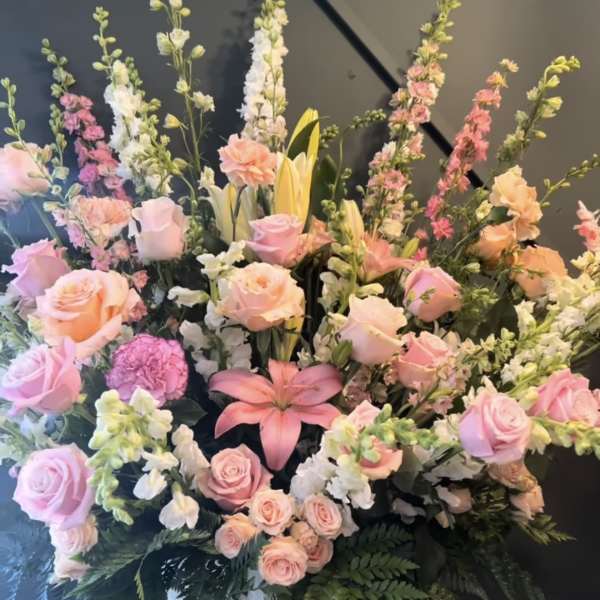 Tall pastel floral arrangement in a white vase with roses, lilies, and snapdragons