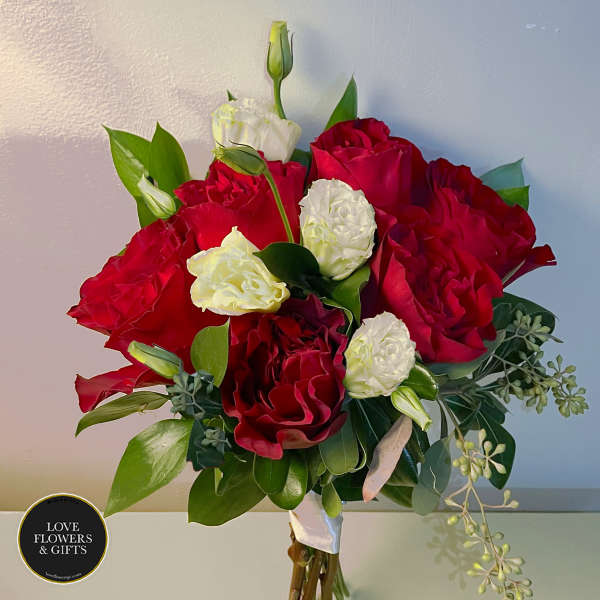 Hand-tied bouquet of red roses with white lisianthus buds and blooms, wrapped with a white ribbon.