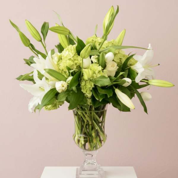 White lilies and green hydrangeas arranged in a clear pedestal vase