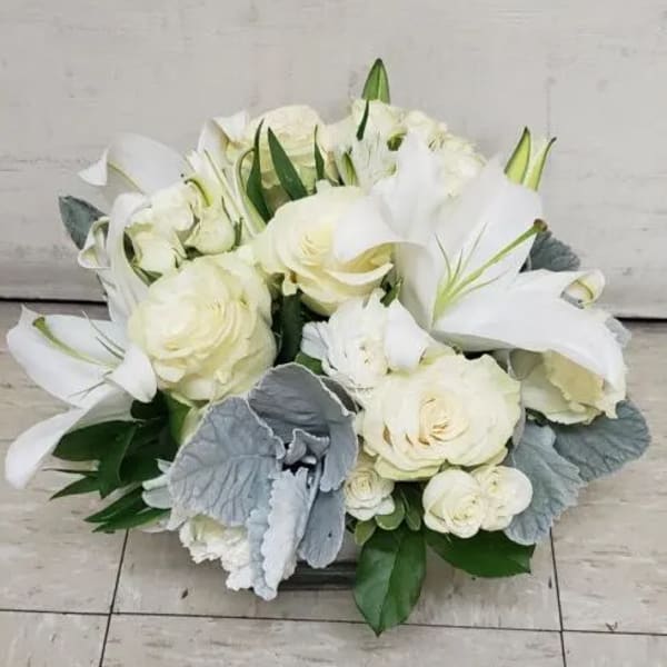 White roses and lilies arranged in a low bouquet with silver foliage