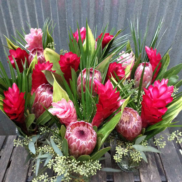 Tropical floral arrangements with red and pink blooms in small glass vases