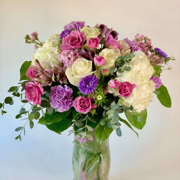 Mixed bouquet of pink, white, and purple flowers in a clear glass vase lined with green leaves