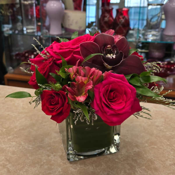 Pink and red roses with a dark orchid in a square glass vase
