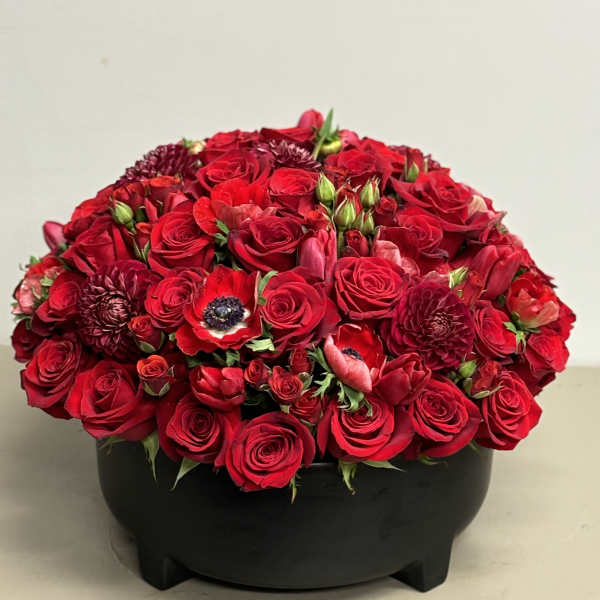 Low dome of red roses and mixed red blooms arranged in a round black bowl.