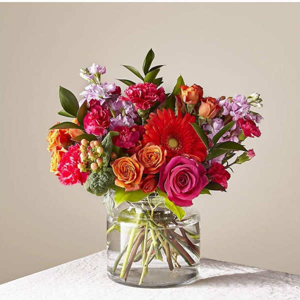 Bright mixed bouquet of pink and orange flowers in a clear glass cylinder vase
