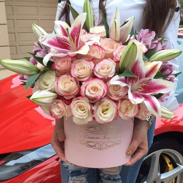 Round pink hatbox of cream roses and pink lilies held in front of a red car
