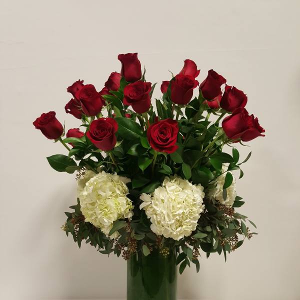Tall arrangement of red roses and white hydrangeas in a clear green-lined glass vase