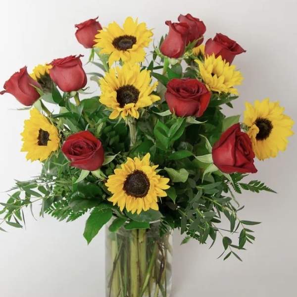 Arrangement of red roses and yellow sunflowers in a clear glass vase