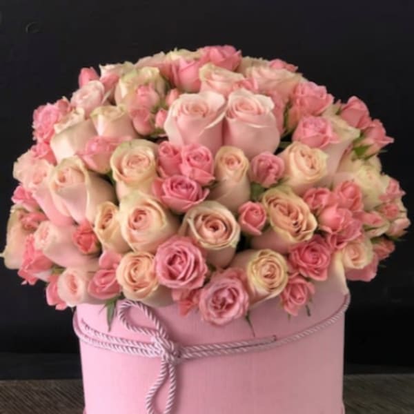 Pink and cream roses arranged in a round pink hat box