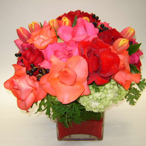 Bouquet of red, pink, and coral roses in a square glass vase