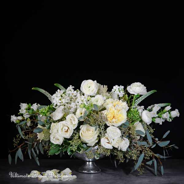 White floral arrangement in a silver pedestal bowl with trailing greenery