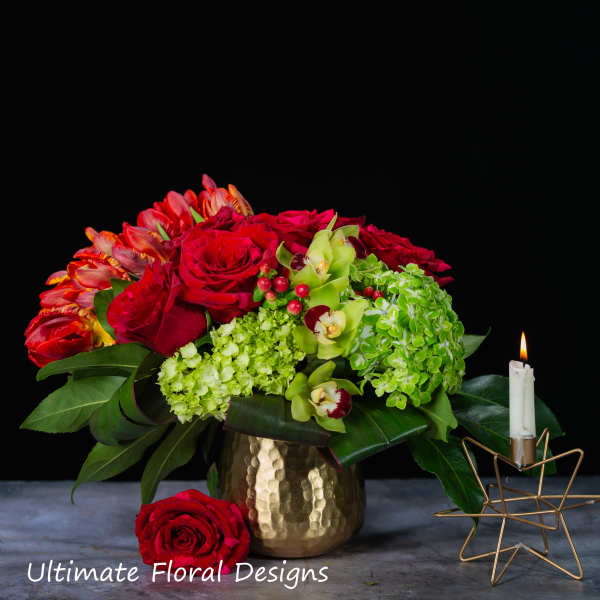 Red roses and green orchids in a gold vase beside a lit candle