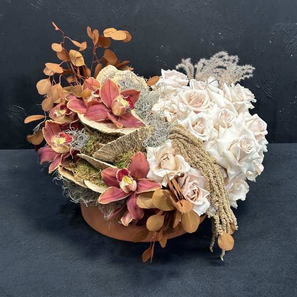 Arrangement of cream roses and burgundy orchids in a low container