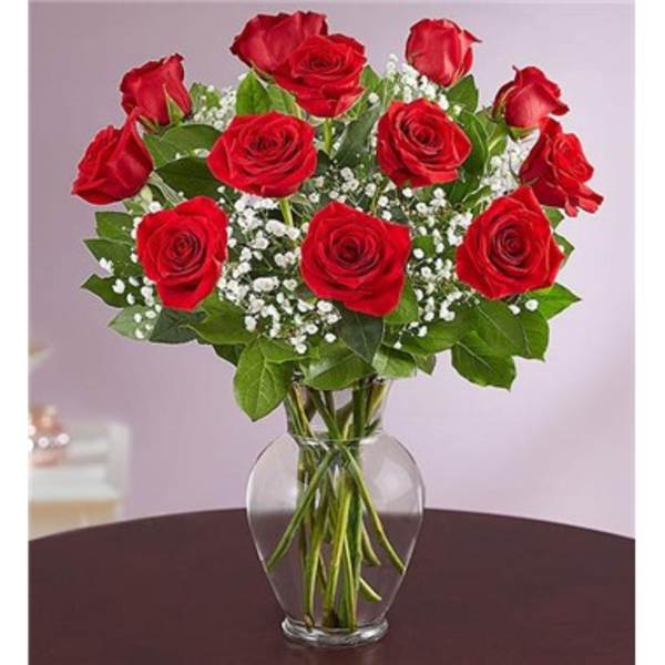 Arrangement of red roses with white filler flowers in a clear glass vase on a dark table