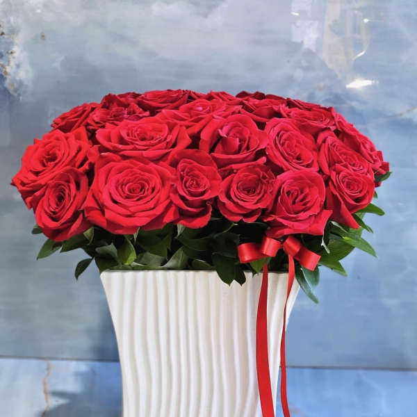 Red roses arranged in a white square vase with a red ribbon