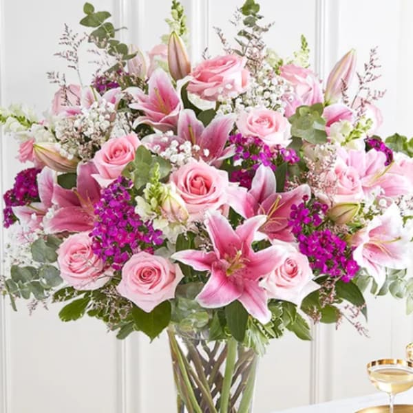 Tall glass vase filled with pink lilies, pink roses, and white and purple filler flowers