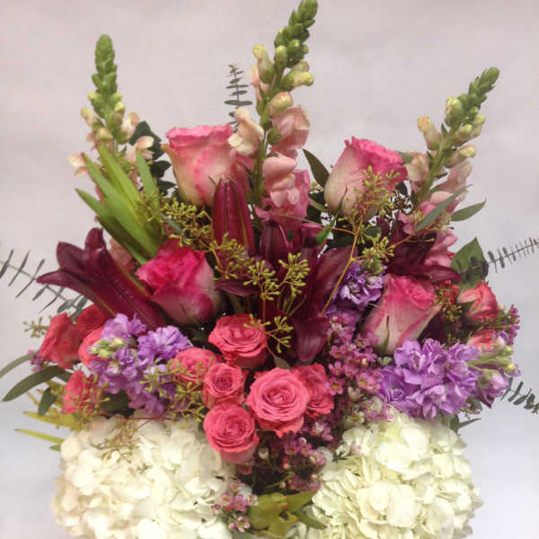 Mixed bouquet of pink roses, purple flowers, and white hydrangeas in a glass vase