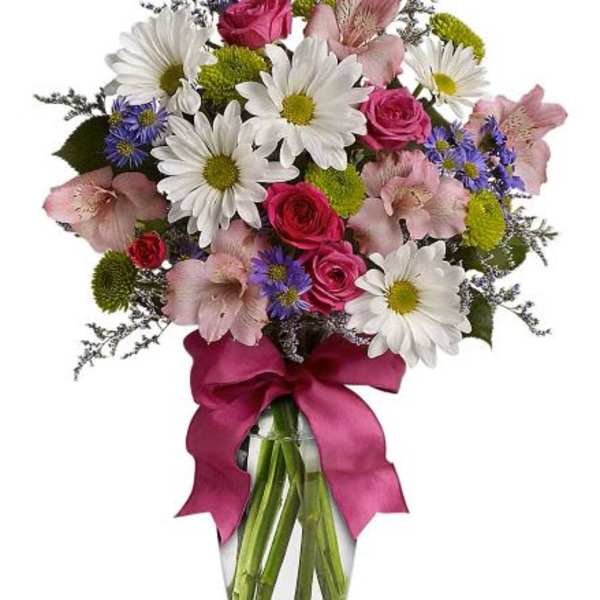 Mixed bouquet of white daisies, pink roses, and other blooms in a glass vase with a fuchsia ribbon bow