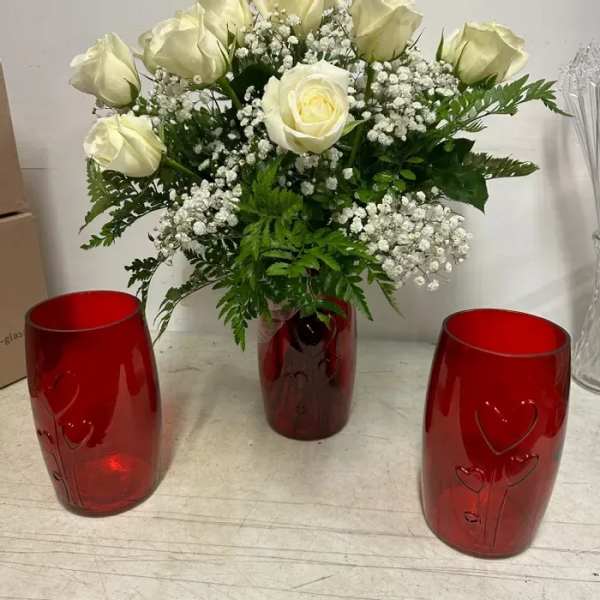 White rose bouquet with baby's breath in a red heart-embossed vase, flanked by two empty matching red vases.