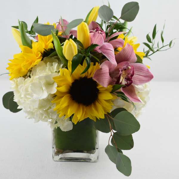 Bouquet of sunflowers, pink orchids, and white hydrangeas in a glass vase