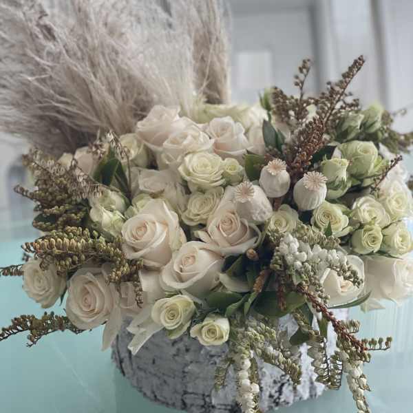 Cream roses arranged in a low stone vase with dried grasses