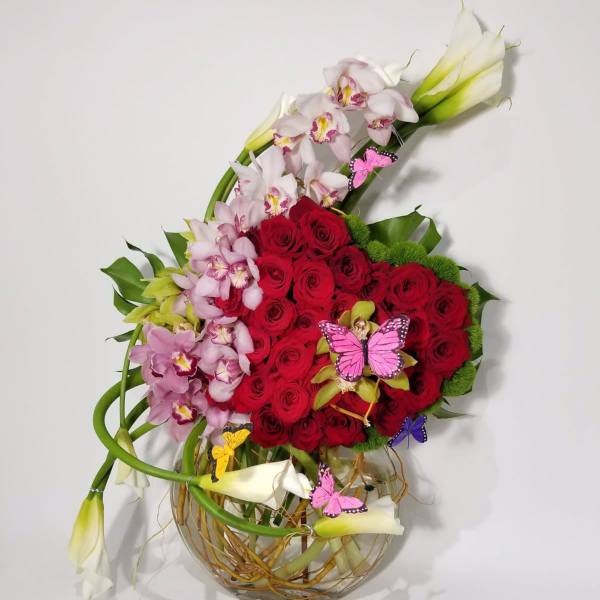 Red roses and pink orchids in a glass vase with butterfly picks
