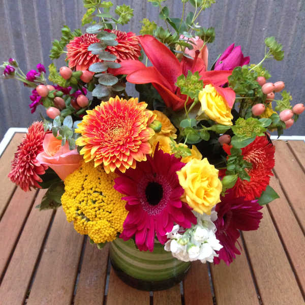 Colorful mixed bouquet in a green glass vase with roses and daisies