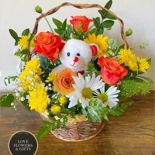 Basket arrangement of orange roses and yellow and white daisies with a small white teddy bear in the center