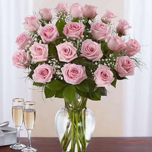 Tall bouquet of pink roses with white filler flowers in a clear glass vase on a table.
