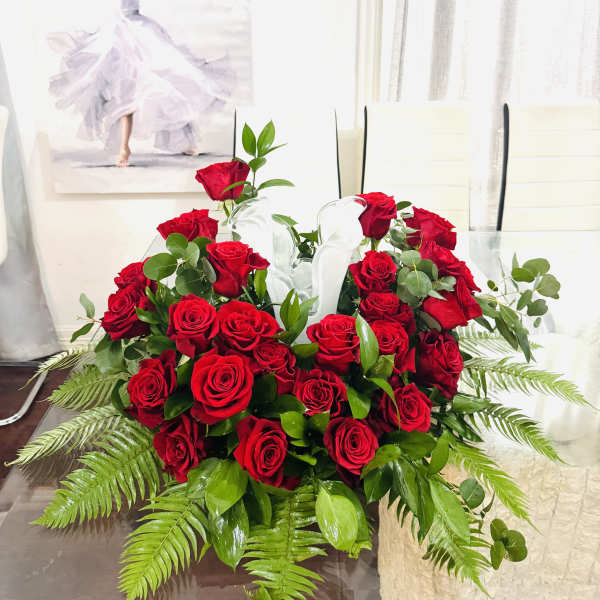 Red rose arrangement in a clear glass vase with fern foliage