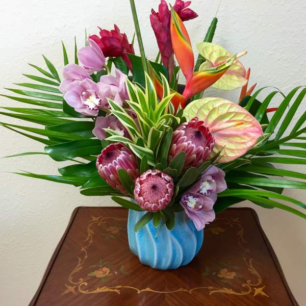 Tropical bouquet with orchids, protea, and anthuriums in a blue vase