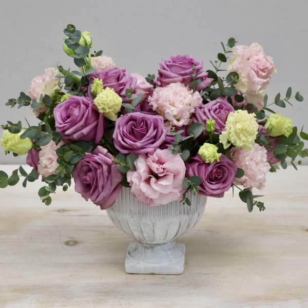 Low centerpiece of purple roses and pastel carnations in a white pedestal bowl