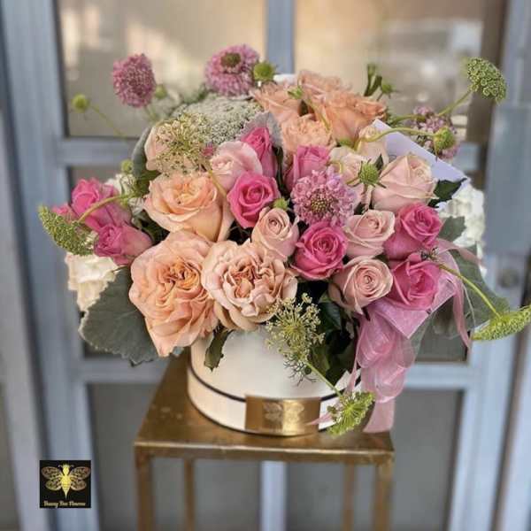 Round hatbox of peach and pink roses with filler blooms on a gold metal stand