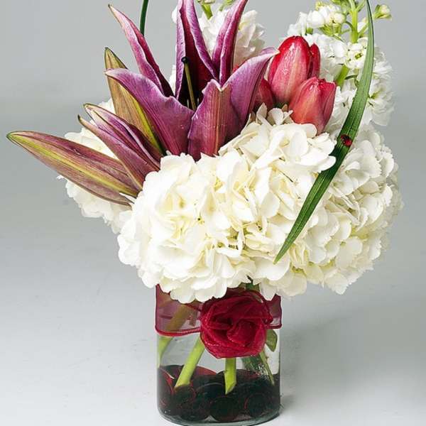 White hydrangeas with purple and pink tulips in a glass vase with a ribbon