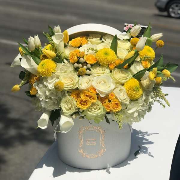 Yellow and white floral arrangement in a gray hatbox